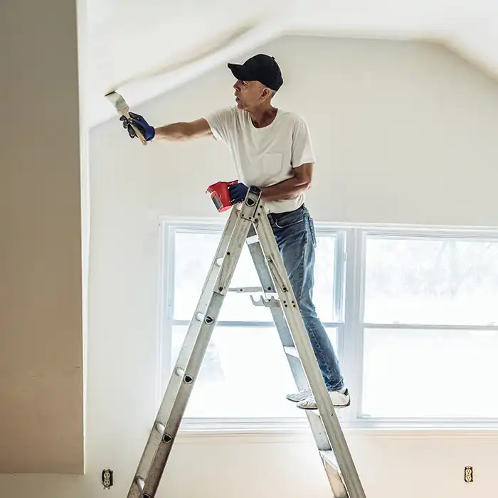 man on ladder painting ceiling and wall